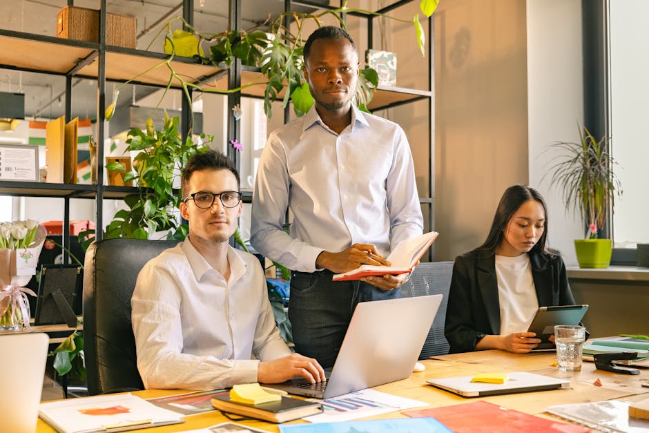 Three professionals collaborate in a well-decorated modern office with plants and laptops.